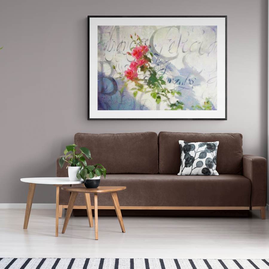 A pintura das rosas emoldurada acima de um sofá marrom, em sala clara com plantas.